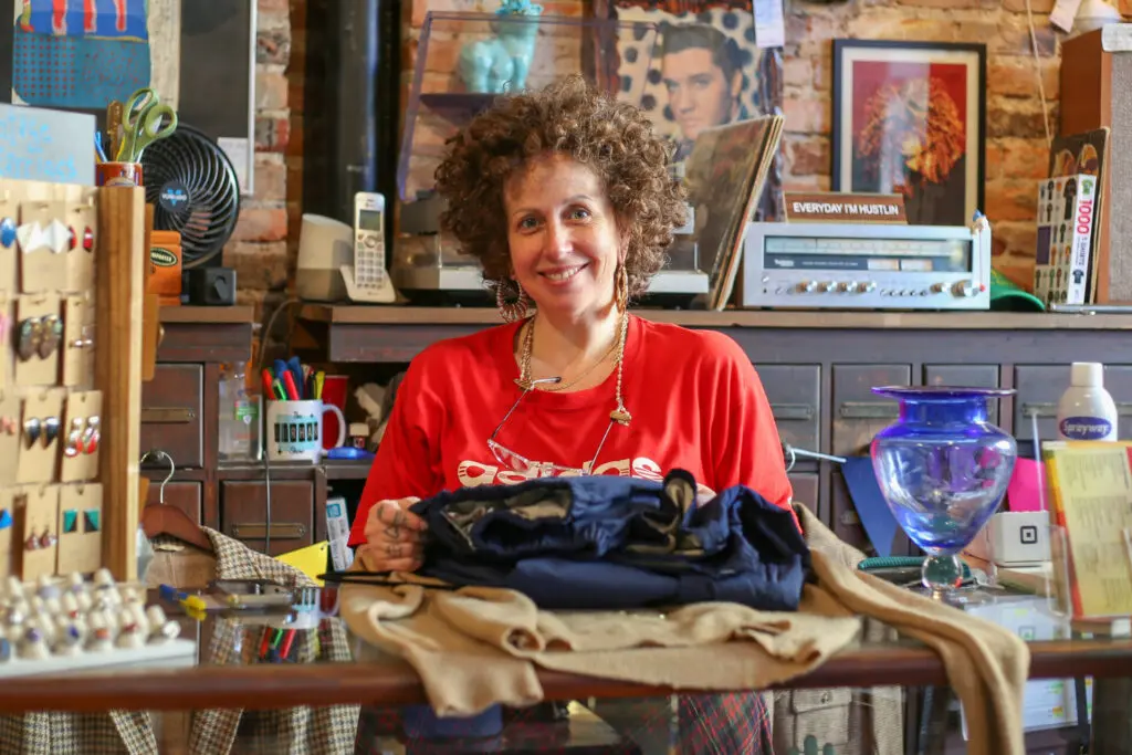 Smiling woman in a red shirt in front of the counter of a vintage store.