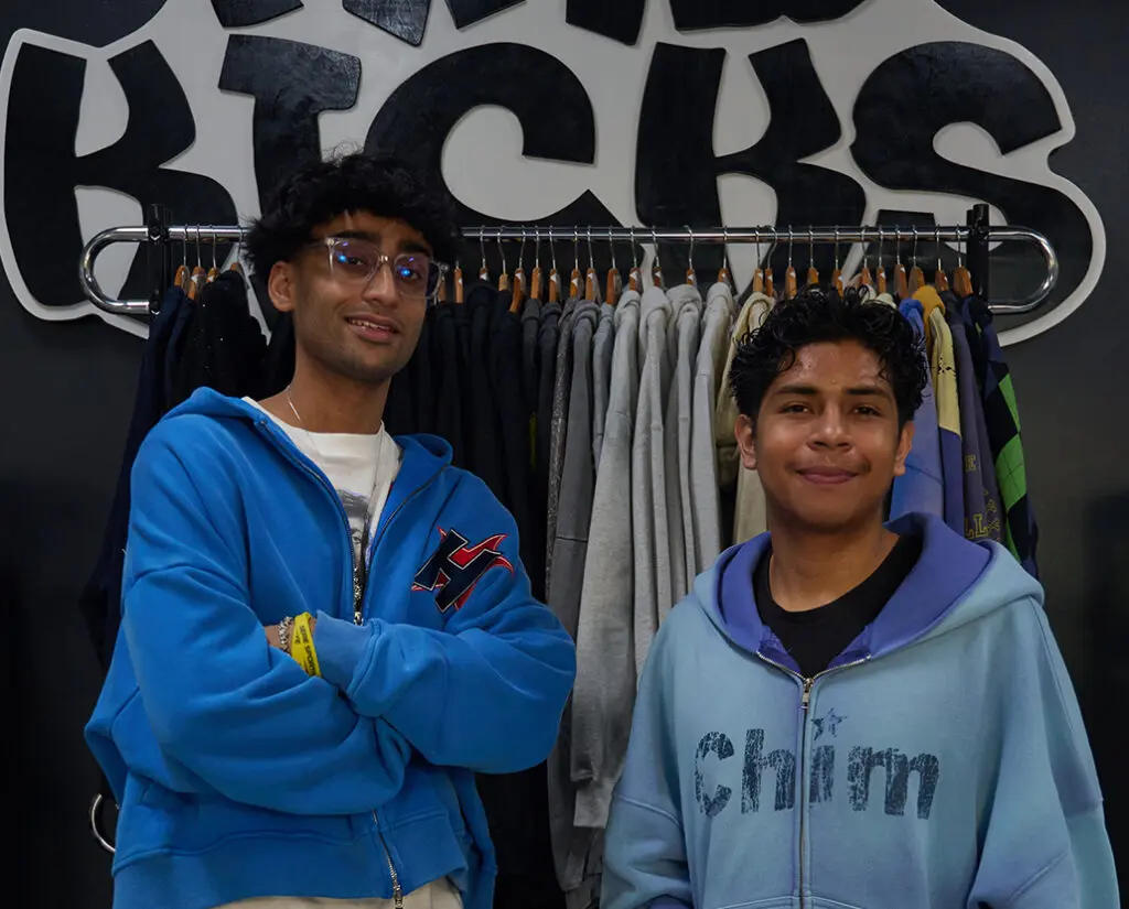 Two young guys in front of a rack of clothing and Mad Kicks sign.