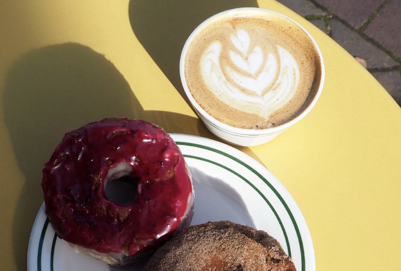 hot latte with latte art and two donuts sitting on yellow table